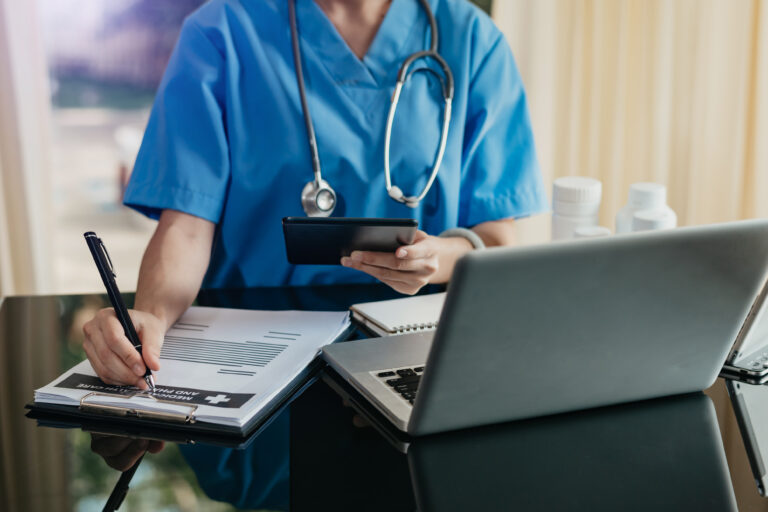 Medical technology concept. Doctor working with mobile phone and stethoscope and digital tablet laptop in modern office at hospital in morning light